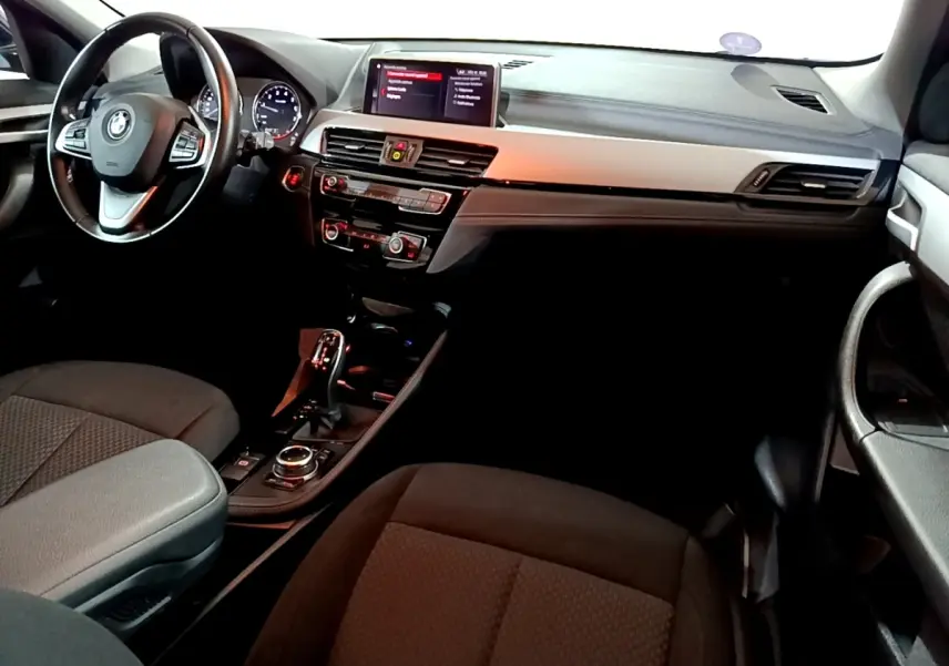 Vue intérieure côté conducteur du BMW X2 sDrive18i Lounge 2023, tableau de bord noir avec écran central et volant cuir.