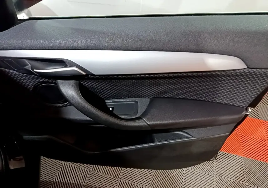 Gros plan sur la porte côté gauche noire avec insert texturé et poignée intérieure argentée du BMW X2 sDrive18i 2023.