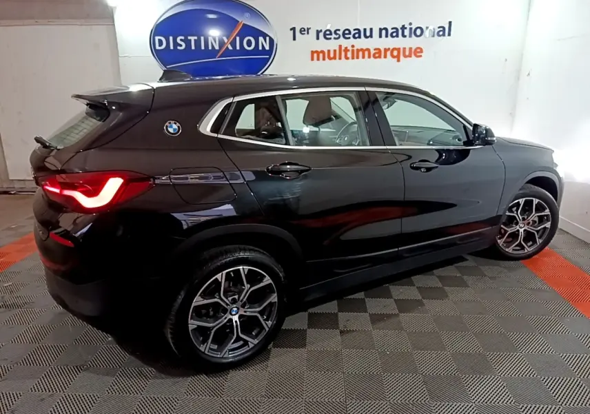 BMW X2 sDrive18i noir en vue de profil côté gauche, avec feux arrière allumés et jantes alliage distinctives.