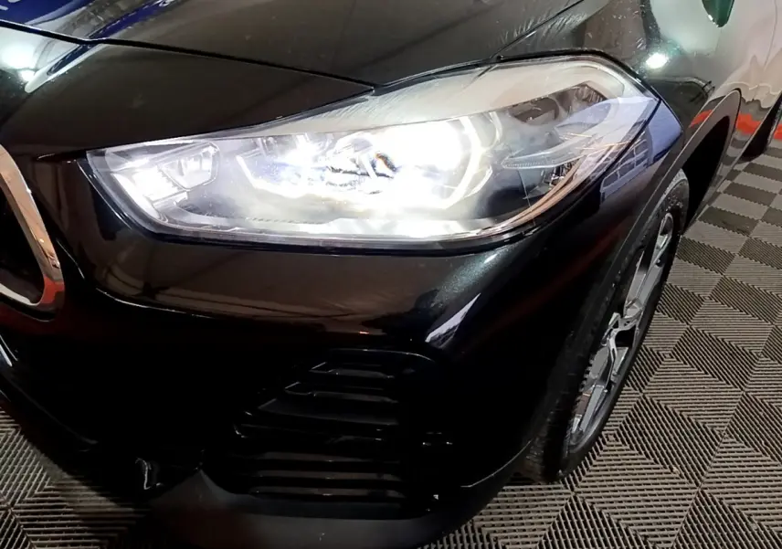 Gros plan sur l'avant droit noir brillant du BMW X2 2023 avec phare LED allumé et jante visible.