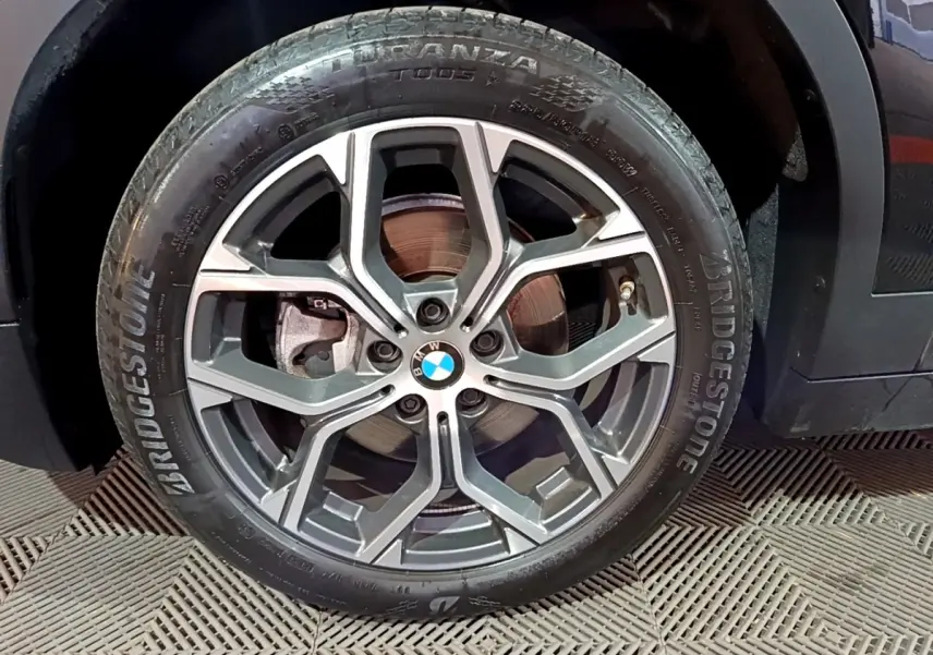 Gros plan sur la roue avant droite d’une BMW X2 noire, jante alliage à design moderne et pneu Bridgestone.