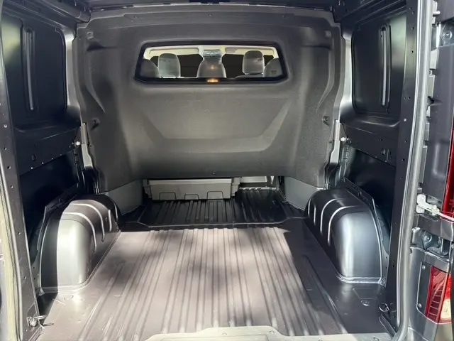 Vue intérieure arrière du fourgon Renault Trafic gris foncé, montrant l'espace de chargement vide avec cloison pleine et banquette avant visible.