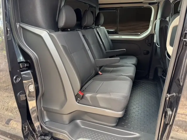 Vue latérale intérieure côté droit du Renault Trafic Fourgon gris foncé, montrant la banquette arrière 3 places avec accoudoir central.