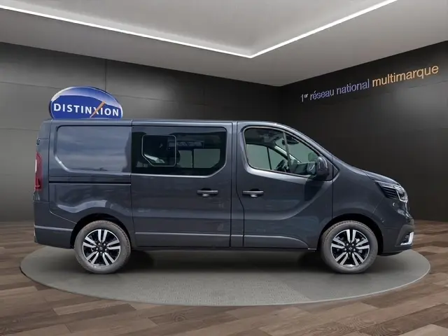 Profil droit du Renault Trafic Fourgon gris foncé 2026 avec jantes alliage et vitres latérales teintées dans un showroom.
