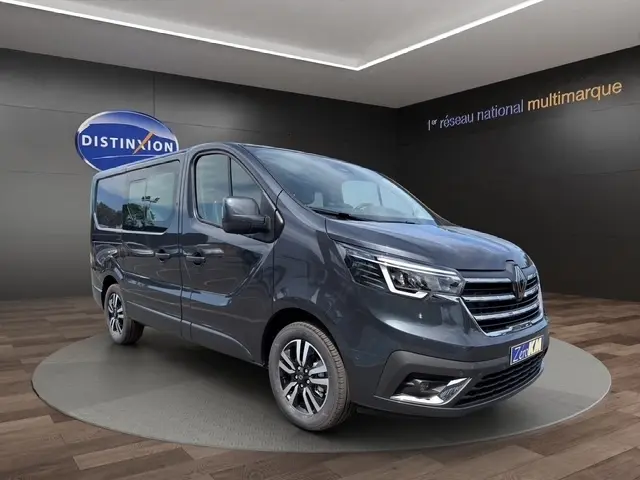 Renault Trafic Fourgon gris foncé en 3/4 avant droit, avec phares LED et jantes alliage visibles, sur fond intérieur showroom.