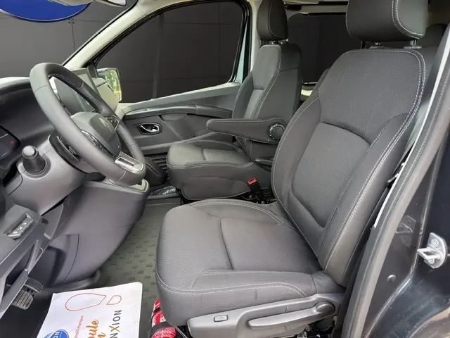 Vue intérieure côté conducteur du Renault Trafic Fourgon gris foncé, avec sièges tissu noirs et accoudoir central avant.