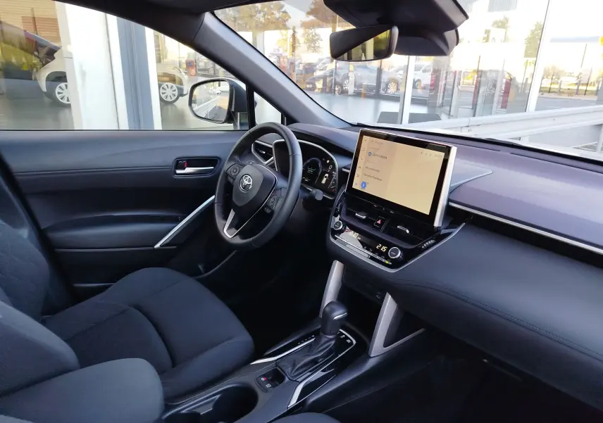 Vue intérieure côté conducteur du Toyota Corolla Cross 2025 gris minéral, avec écran tactile central et volant multifonction.