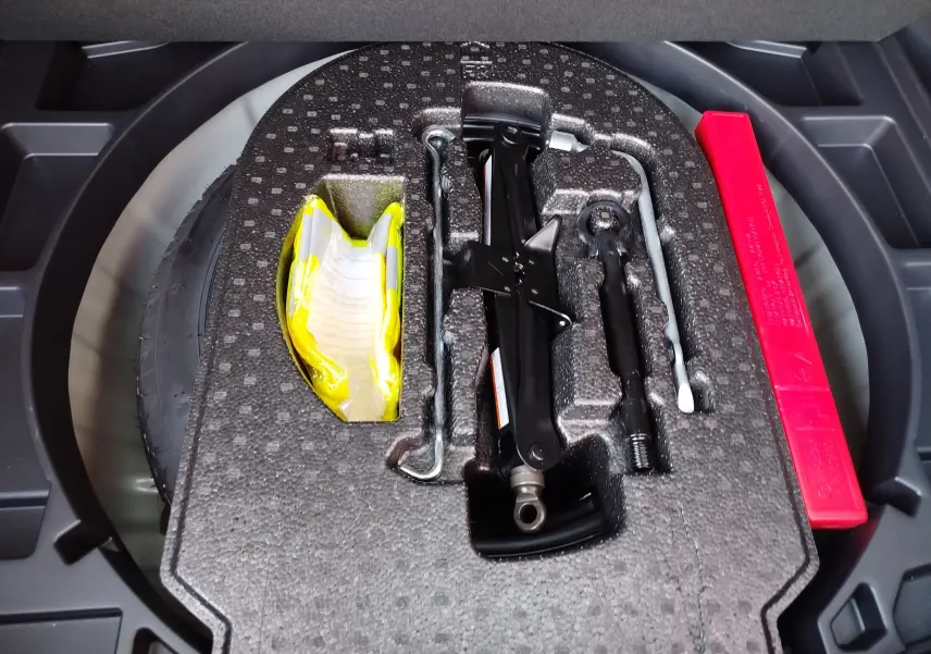 Vue rapprochée du coffre d'une Toyota Corolla Cross 2025 gris minéral, montrant la roue de secours et les outils de dépannage.