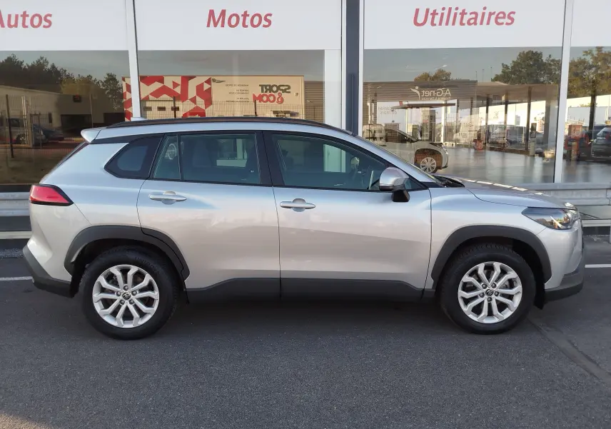Profil droit d'un Toyota Corolla Cross gris minéral 2025, version 1.8 140ch Dynamic avec jantes alliage et toit noir.