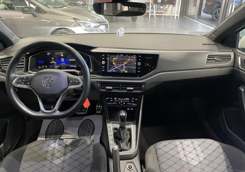 Vue intérieure avant de la Volkswagen Polo 2024 R-Line avec tableau de bord numérique et sellerie tissu gris à motifs.