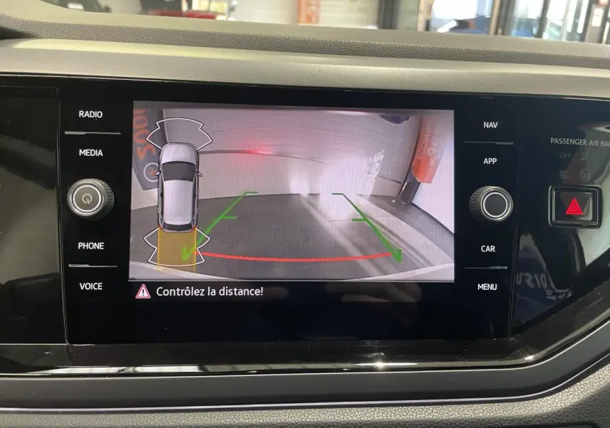 Écran tactile intérieur montrant la caméra de recul d'une Volkswagen Polo blanche, vue arrière avec guidage de stationnement.