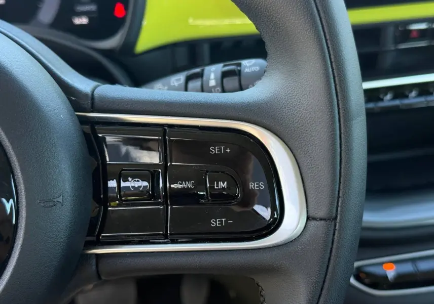 Gros plan sur les commandes multifonctions du volant noir de la FIAT 500 électrique jaune, côté gauche.