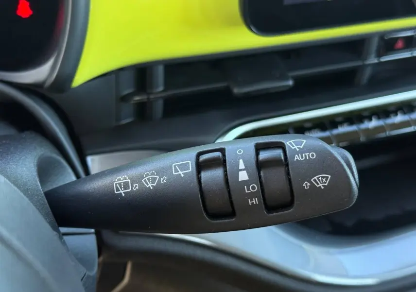 Gros plan sur la commande d'essuie-glace du volant, avec tableau de bord jaune vif en arrière-plan, Fiat 500 électrique 2024.