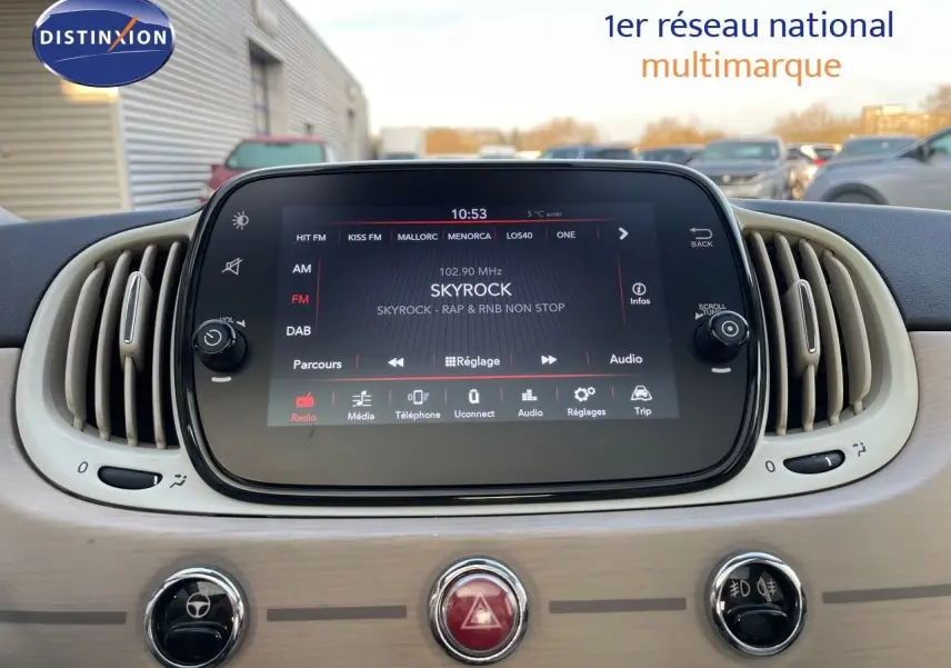 Tableau de bord de Fiat 500 blanc 2022 avec écran tactile central affichant la radio Skyrock, entouré de grilles d'aération ovales.