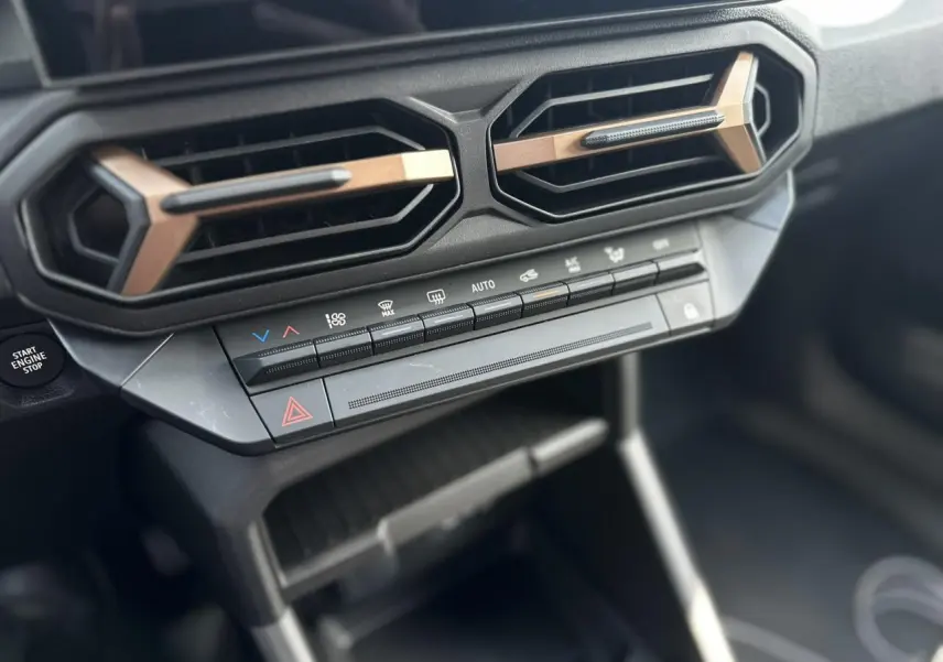 Détail de la console centrale du Dacia Duster 2025 gris, avec commandes climatisation et aérateurs hexagonaux bronze.