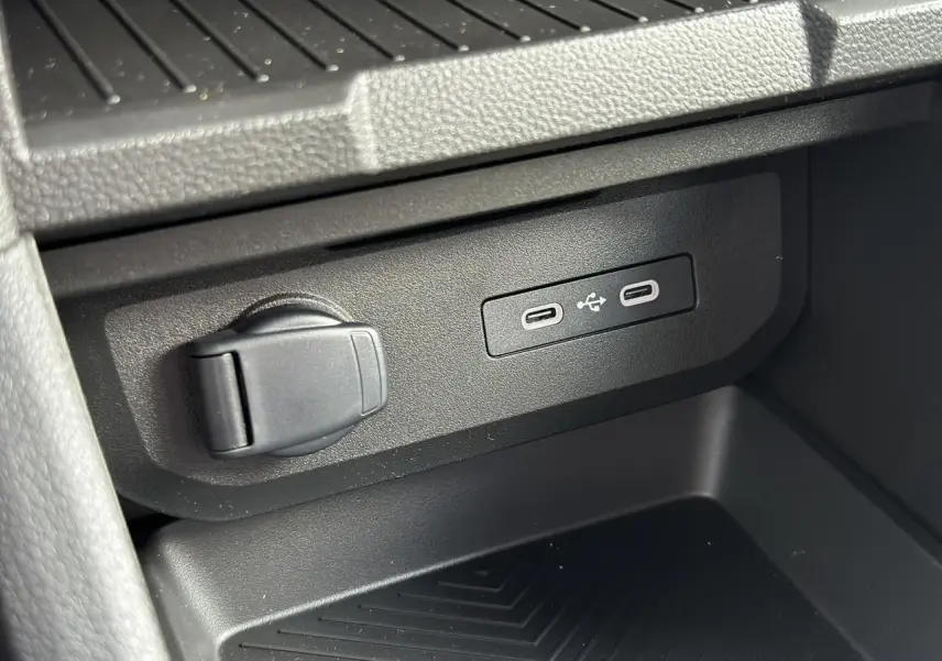 Prise USB et prise 12V noires en gros plan dans l'espace de rangement central du Dacia Duster Gris Schiste 2025.