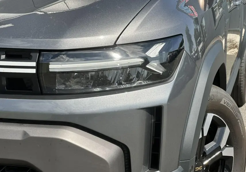 Gros plan sur le phare avant droit et la jante alliage du Dacia Duster 2025 gris schiste, version ECO-G 100 Extrême.