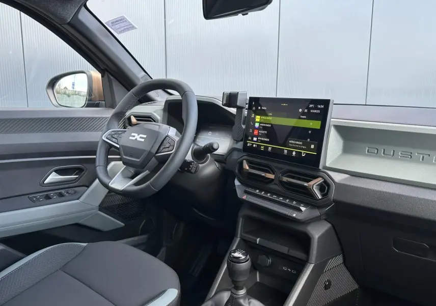 Vue intérieure côté conducteur du Dacia Duster 2025 avec tableau de bord digital et écran tactile central.