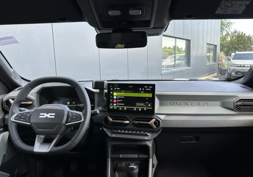 Tableau de bord du Dacia Duster 2025 gris, vue frontale du volant et écran tactile central avec commandes modernes.