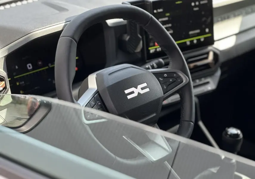 Vue rapprochée du volant multifonction noir et du tableau de bord digital du Dacia Duster 2025 gris Schiste.