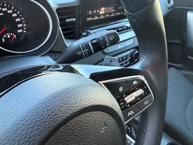 Gros plan sur le volant cuir avec commandes multifonctions et palettes de la Kia CEE'D 2024, intérieur moderne gris et noir.