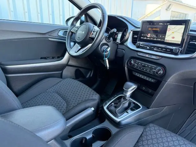 Intérieur de la Kia CEE'D 2024 côté conducteur, avec volant multifonction, écran tactile et levier de boîte automatique.