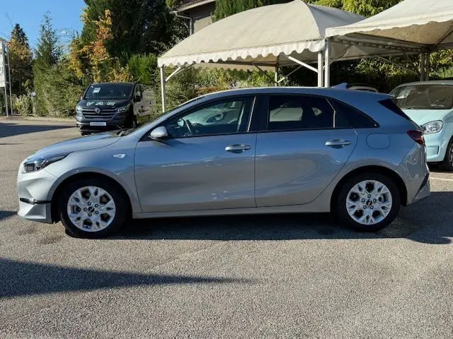 Profil côté gauche d'une KIA CEE'D argent lunaire 2024 stationnée en extérieur sous un auvent blanc.