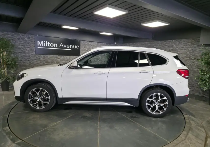 Vue latérale droite d'un BMW X1 sDrive 18d blanc avec jantes alliage 18 pouces style 579 dans un showroom.