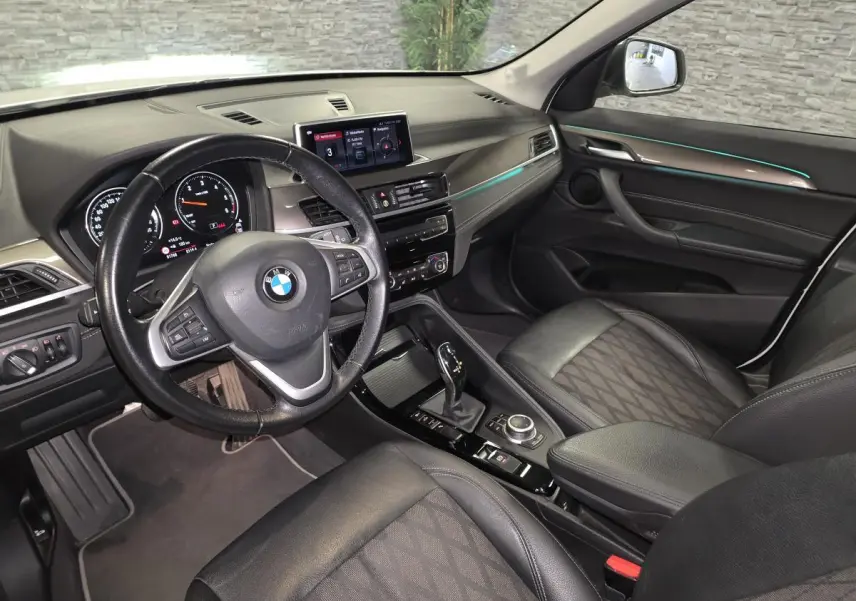 Vue intérieure côté conducteur du BMW X1 sDrive 18d 2022, sellerie cuir tissu noire avec éclairage d'ambiance bleu.