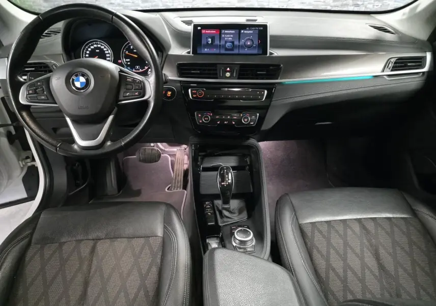 Vue intérieure avant du BMW X1 sDrive 18d 2022, tableau de bord noir avec écran central et volant cuir multifonctions.