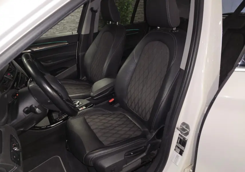 Vue intérieure côté conducteur du BMW X1 blanc 2022, sièges avant en cuir et tissu avec surpiqûres contrastantes.