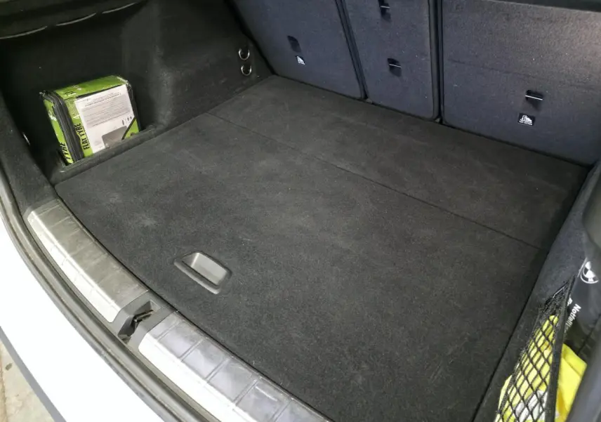 Vue intérieure du coffre noir du BMW X1 blanc 2022 avec tapis et rangements latéraux visibles.