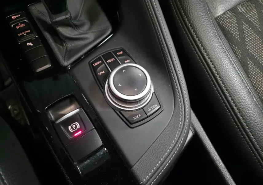 Gros plan sur la console centrale noire avec molette iDrive et commandes de la BMW X1 sDrive 18d BVA Sport xLine 2022.