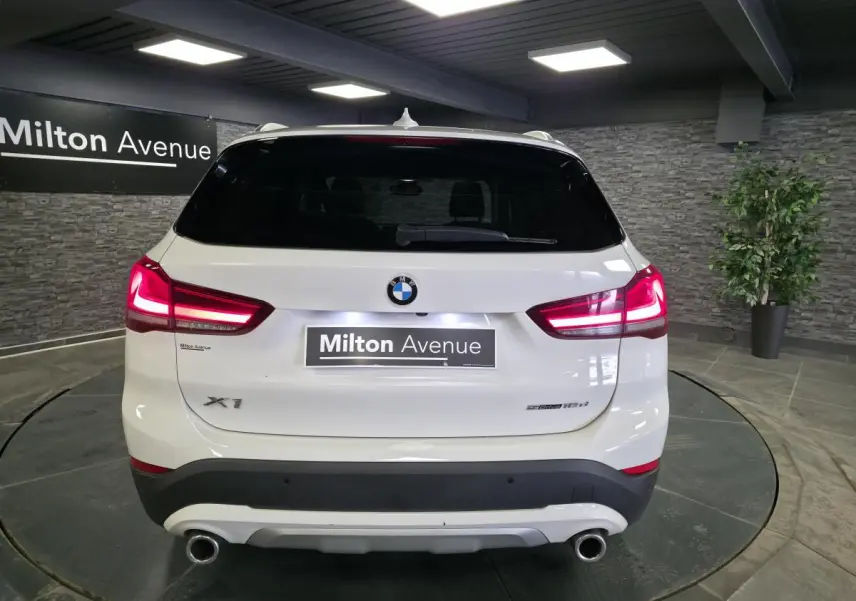 Vue arrière d'un BMW X1 blanc avec feux allumés et double sortie d'échappement chromée dans un showroom.