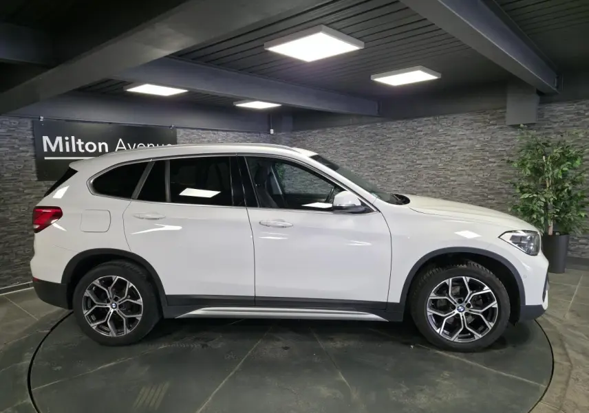 BMW X1 sDrive 18d blanc vue de profil côté gauche, avec jantes alliage 18 pouces et bas de caisse noirs.