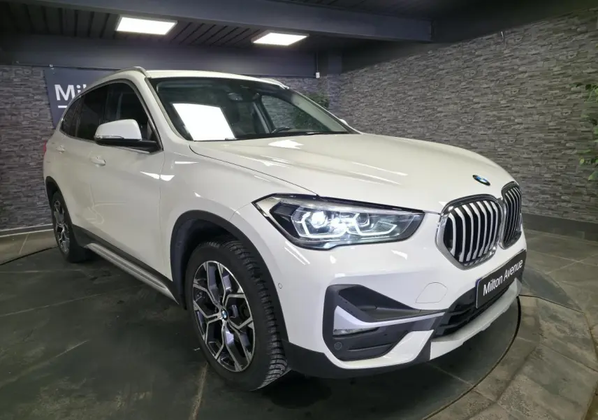 BMW X1 sDrive 18d blanc vue 3/4 avant droit, avec phares LED allumés et jantes alliage 18 pouces style 579.
