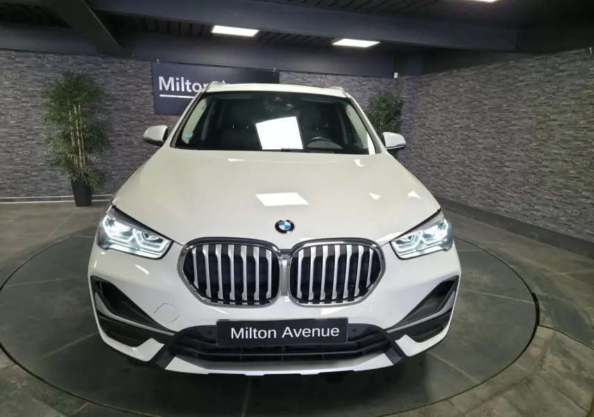 Vue de face d’un BMW X1 sDrive 18d blanc avec calandre double haricot et phares LED allumés en showroom.