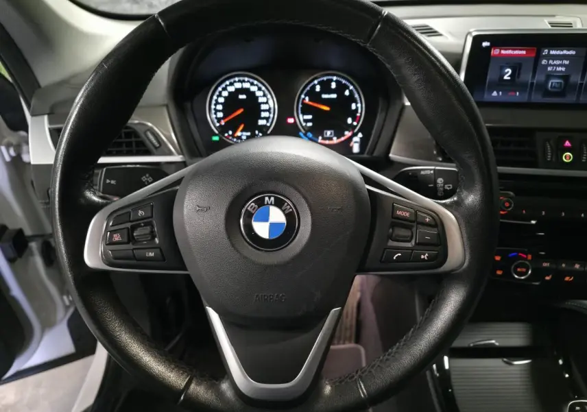 Vue intérieure centrée sur le volant cuir noir du BMW X1 2022 avec tableau de bord et écran multimédia visible à droite.