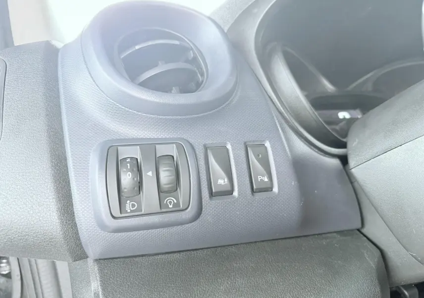 Détail des commandes d'éclairage et d'assistance au stationnement sur tableau de bord gris foncé d'Opel Vivaro blanc.