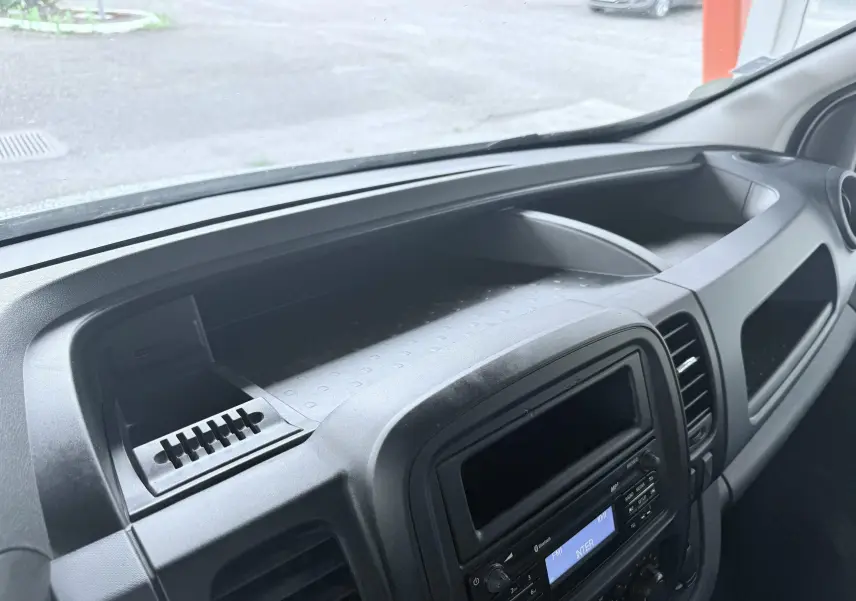 Tableau de bord noir de l'Opel Vivaro 2018 vu de côté, avec console centrale et rangement supérieur visible.