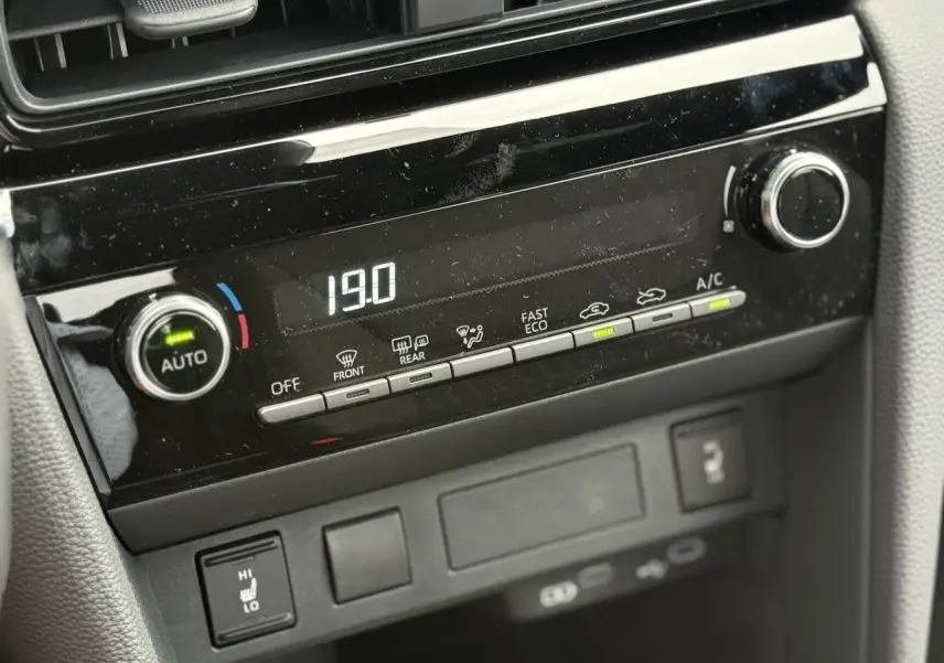 Gros plan sur la console centrale noire de la Toyota Yaris Cross 2026 montrant la climatisation automatique réglée à 19°C.