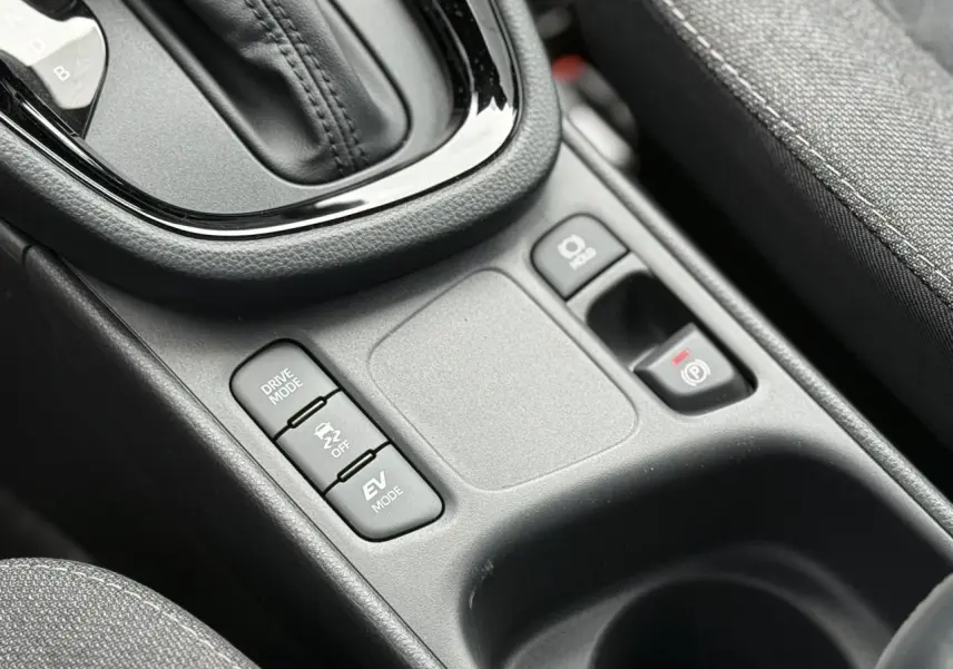 Gros plan sur la console centrale noire de la Toyota Yaris Cross 1.5 Hybrid 116 Design avec boutons Drive Mode et frein électronique.