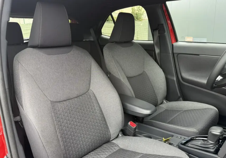 Vue intérieure des sièges avant gris de la Toyota Yaris Cross 1.5 Hybrid 116 Design rouge, avec accoudoir central.