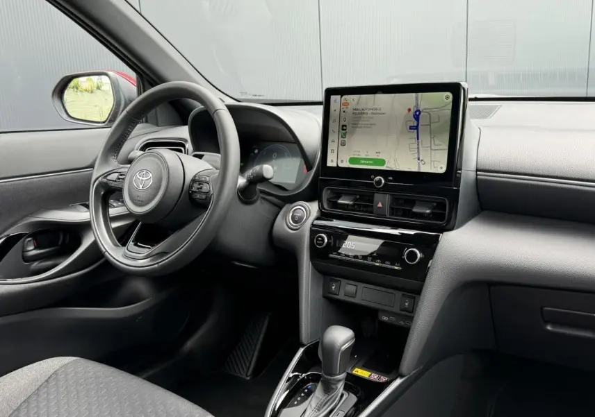 Vue intérieure côté conducteur de la Toyota Yaris Cross rouge intense, avec tableau de bord numérique et écran tactile central.