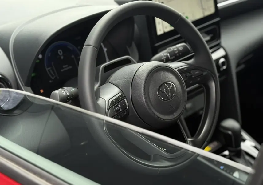 Vue rapprochée du volant cuir noir et du tableau de bord numérique de la Toyota Yaris Cross rouge intense.