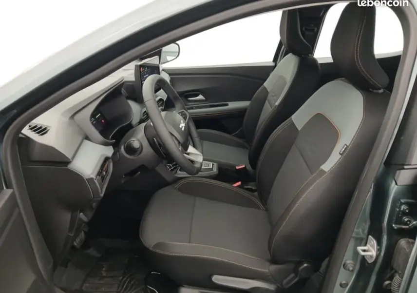 Vue intérieure côté conducteur de la Dacia Sandero verte 2026, sièges noirs avec surpiqûres orange et volant multifonctions.
