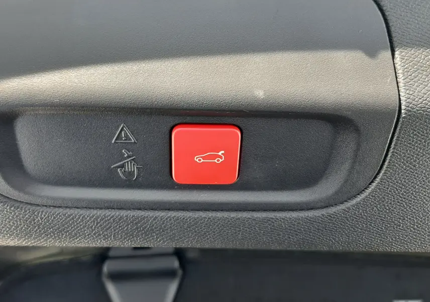 Gros plan sur le bouton rouge d'ouverture électrique du coffre dans l'habitacle d'une Peugeot 408 gris selenium.