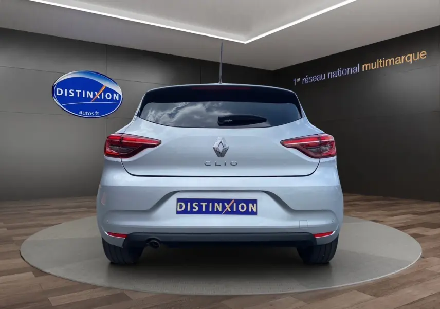 Vue arrière d'une Renault Clio V gris Highland 2023 avec feux LED et plaque Distinxion en showroom.