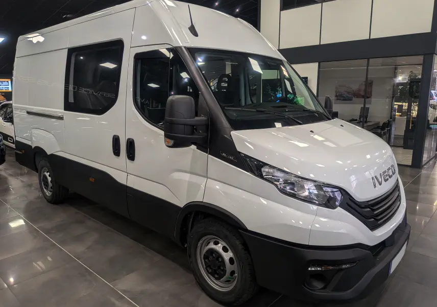 Fourgon Iveco Daily blanc vu en 3/4 avant droit dans un showroom avec vitres teintées et pare-chocs noirs.