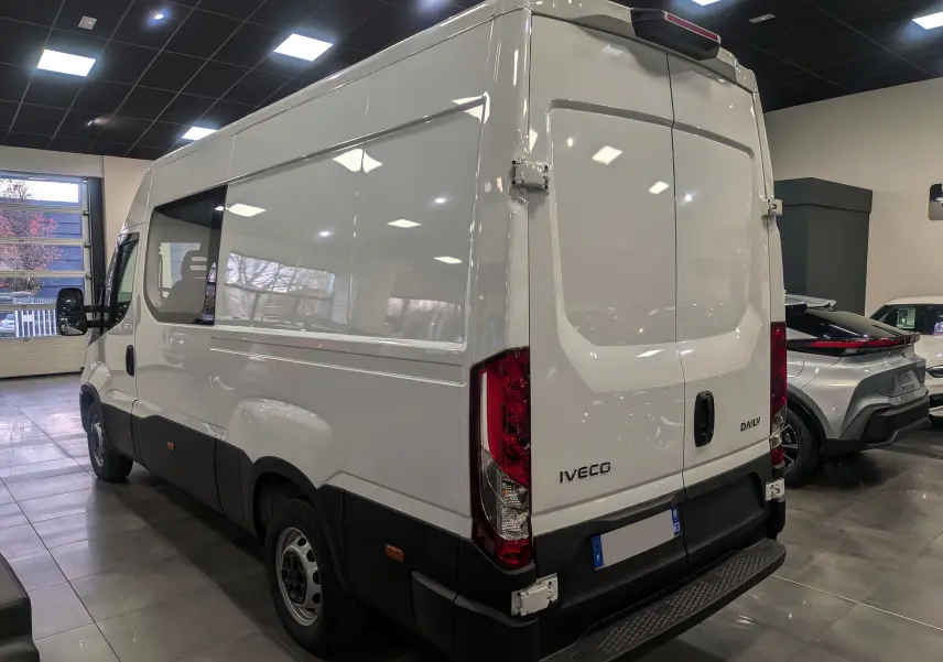 Vue 3/4 arrière droite d'un fourgon Iveco Daily blanc 2025 avec portes arrière fermées dans un showroom.